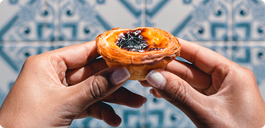 O que e onde comer em Lisboa: pastel de nata português segurado com as mãos em frente a azulejos tradicionais